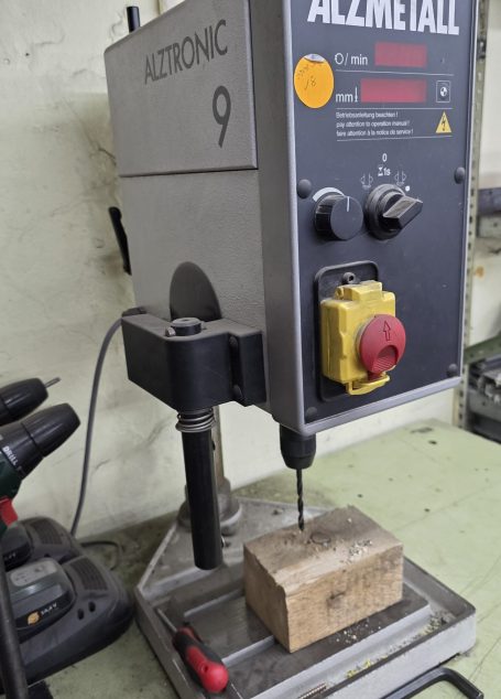Bohrmaschine der Marke Alzmetall, auf einem Tisch mit einem Holzblock.